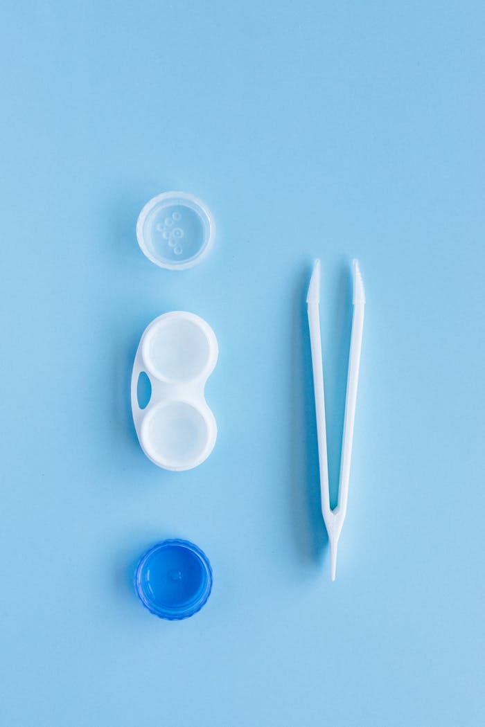 gallery-4 A contact lens kit featuring a lens case and tweezers arranged on a blue background in flat lay style.